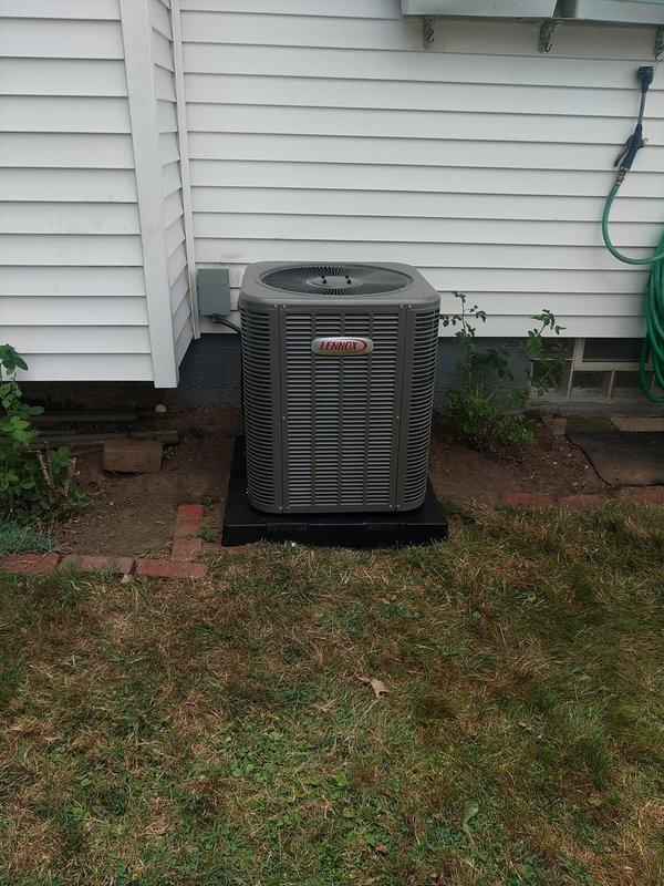 Completed second phase of residential air conditioning system installation. Installed Lennox outdoor condensing unit on composite pad with proper leveling and clearances from structure. Unit positioned against exterior wall with white vinyl siding, secured disconnect switch with 20-amp Bussmann fuses, and verified all electrical connections per manufacturer specifications and local code requirements.