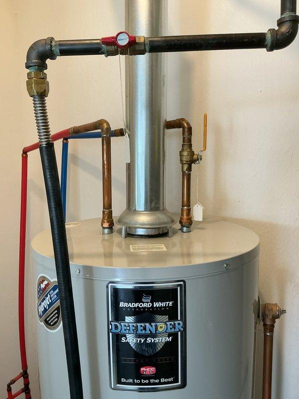 Responded to no hot water complaint at 8-year-old residence. Upon inspection, determined Bradford White tanked water heater pilot light would not remain lit, rendering unit inoperable. Evaluated existing water heater system including all plumbing connections, copper piping, brass fittings, and safety components. Documented current installation configuration showing Defender Safety System unit with associated gas line, water supply lines, pressure relief valve, and venting system. Provided free estimate for complete Bradford White tanked water heater replacement due to pilot light failure preventing hot water production throughout home.
