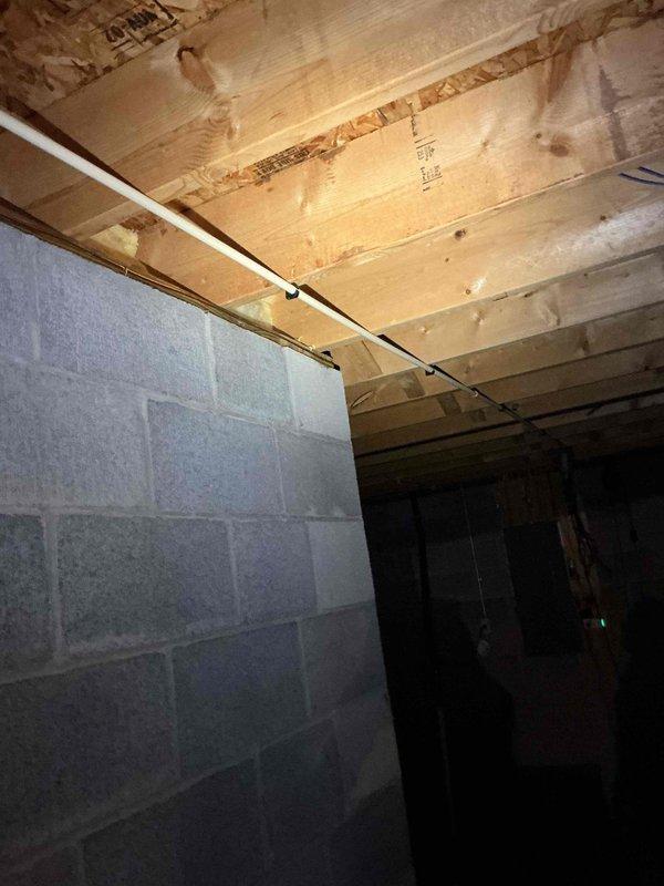 Conducted on-site electrical assessment for Generac generator installation. Evaluated unfinished basement area with exposed floor joists and concrete block foundation walls to determine optimal equipment placement and electrical routing. Inspected existing utility infrastructure including water meter and copper supply lines to identify potential conflicts with proposed generator transfer switch and electrical panel connections. Documented structural conditions, available clearances, and existing PVC plumbing runs to ensure code-compliant installation pathway for generator feeder cables and gas supply lines. Assessed electrical service entry point and determined feasibility for automatic transfer switch integration with existing electrical distribution system.