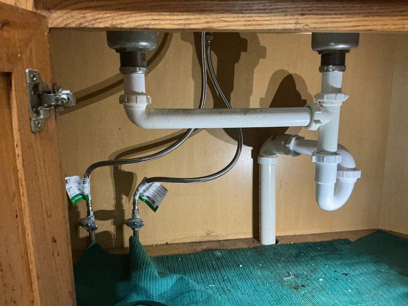 Responded to service call for leaking under kitchen sink. Upon inspection, identified loose tailpiece connections and cracked PVC piping in the P-trap assembly of double-sink drainage system. Tightened all threaded connections at basket strainers and tailpieces. Replaced damaged sections of white PVC drain pipe and P-trap components. Verified all supply line connections at shut-off valves were secure with no leaks present. Tested both drains under full water flow to confirm proper drainage and verified all connections remained dry and leak-free.