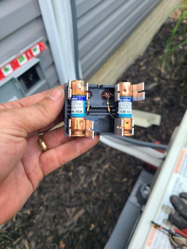Completed installation of single-head ductless mini-split system with outdoor condenser unit mounted on concrete pad and refrigerant line set routed vertically along exterior wall. Installed disconnect box and associated electrical components, replaced damaged 25-amp fuse block that showed signs of electrical failure and burn damage between terminals.