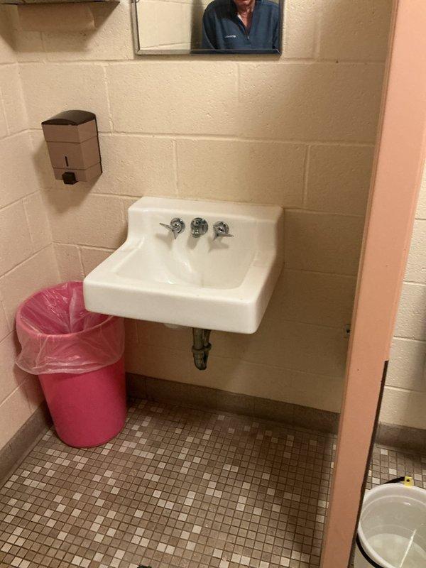 Responded to service call for bathroom fixture assessment in commercial restroom facility. Evaluated existing wall-mounted sink with three-handle faucet configuration, inspecting visible supply lines and chrome P-trap assembly for potential replacement. Assessed urinal flush valve system requiring new flush kit installation. Documented garbage disposal requirement for estimate preparation. Noted visible water damage and staining at tile base along wall perimeter, indicating potential moisture intrusion issues. Photographed existing fixture conditions, plumbing connections, and deteriorated areas to support comprehensive estimate for fixture replacements and necessary repairs.