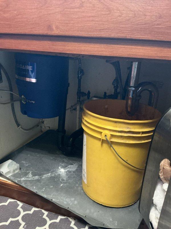 Responded to water leak under kitchen sink. Upon arrival, found dime-sized hole in the gooseneck (drain tailpiece) causing active leak into cabinet. Assessed damage to cabinet interior and placed bucket to contain water. Recommended replacement of corroded drain assembly to prevent further water damage.