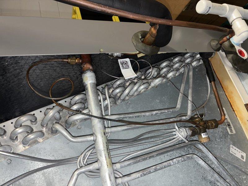 Responded to no-cooling complaint on 9-year-old Lennox central air conditioning system. Upon arrival, confirmed indoor blower, outdoor fan, and compressor were all operating, but both refrigerant lines remained at ambient temperature after extended run time with no heat rejection at condenser and no cooling delivered indoors. Diagnosed complete loss of refrigerant charge due to leak in evaporator coil. Located active leak at coil connection point. Recovered remaining trace refrigerant from system, replaced failed evaporator coil assembly, pressure tested system to 350 PSI and held for one hour with no pressure drop, evacuated system to 500 microns, and recharged with manufacturer-specified refrigerant to proper subcooling and superheat levels. Replaced deteriorated line insulation on suction line. Verified proper system operation with appropriate temperature split across evaporator coil and warm discharge air at condenser. System restored to full cooling capacity.