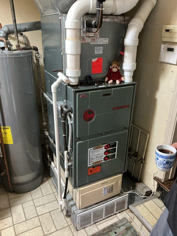 Completed full HVAC system installation including 90% efficiency furnace, air conditioning unit, and humidifier in residential basement utility room. Installed new furnace with proper venting using white PVC piping configured with multiple elbows for exhaust and intake termination. Connected furnace to existing ductwork and established electrical connections. Mounted and positioned Rheem brand air conditioning condenser unit at exterior location. Integrated humidifier into HVAC system for whole-home humidity control. Verified all PVC venting meets code requirements with proper slope and support. Tested system operation including furnace ignition sequence, blower motor function, and thermostat communication. Confirmed AC refrigerant lines properly connected and system charged to manufacturer specifications. Ensured all safety labels and documentation affixed to equipment. System tested and operational upon completion.
