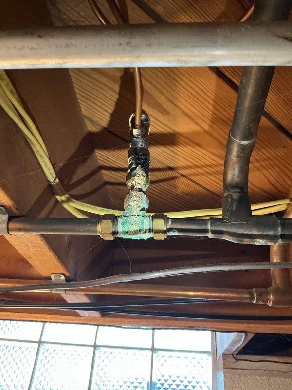 Responded to urgent gas leak investigation in 72-year-old residential property following gas company referral. Conducted comprehensive pressure testing and leak detection throughout plumbing system, focusing on aged copper piping infrastructure and corroded brass valve fittings located in attic/ceiling space. Identified significant oxidation and turquoise-green patina buildup on central valve assembly connecting multiple copper pipe sections, indicating advanced corrosion requiring immediate attention. Inspected basement mechanical room piping including copper lines, insulated pipes, and PVC drainage system to isolate leak source. Documented deteriorated valve condition and compromised connections affecting hot water availability.