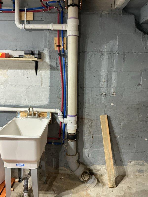 Responded to complaint of intermittent sewer odor in 1917-era residence. Upon inspection, identified potential issues with plumbing venting system and drain trap configurations. Examined basement utility area plumbing stack, including white PVC drain/vent lines and PEX water supply manifold system. Inspected under-sink cabinet plumbing, verifying P-trap assembly and connections for proper seal integrity. Photographed existing plumbing installations showing vertical drain stack with manifold connections and under-cabinet trap configuration with backflow prevention device. Advised homeowner on potential causes of sewer gas infiltration, including dry traps, compromised vent stack, or deteriorated wax ring seals at fixtures. Recommended monitoring situation and provided guidance on maintaining proper trap seals through regular fixture use.