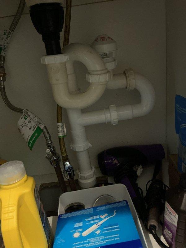 Responded to complaint of intermittent sewer odor in 1917-era residence. Upon inspection, identified potential issues with plumbing venting system and drain trap configurations. Examined basement utility area plumbing stack, including white PVC drain/vent lines and PEX water supply manifold system. Inspected under-sink cabinet plumbing, verifying P-trap assembly and connections for proper seal integrity. Photographed existing plumbing installations showing vertical drain stack with manifold connections and under-cabinet trap configuration with backflow prevention device. Advised homeowner on potential causes of sewer gas infiltration, including dry traps, compromised vent stack, or deteriorated wax ring seals at fixtures. Recommended monitoring situation and provided guidance on maintaining proper trap seals through regular fixture use.