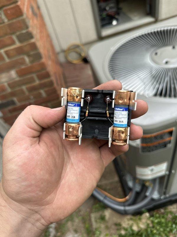 Completed installation of Lennox air conditioning system with matching evaporator coil at residential property. Unit positioned on wooden platform base adjacent to brick and vinyl siding exterior, with proper electrical connections including 30-amp fuses and conduit routing to outdoor disconnect. All refrigerant lines connected, system tested, and confirmed operational.