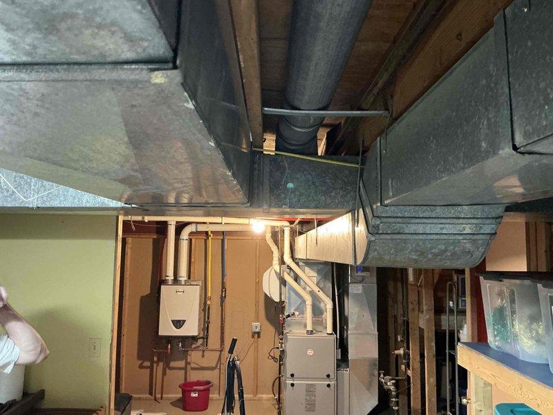 Completed estimate for reworking main trunk ductwork serving approximately half of the residence. Assessed existing basement HVAC distribution system, including large flexible metallic duct connections, rectangular metal plenum transitions, and main trunk line routing through exposed ceiling joists. Documented current condition of ductwork showing dust accumulation and aging insulation. Evaluated integration with existing mechanical equipment including furnace unit and water heater. Photographed ductwork configuration, support systems, and clearances for comprehensive estimate preparation.