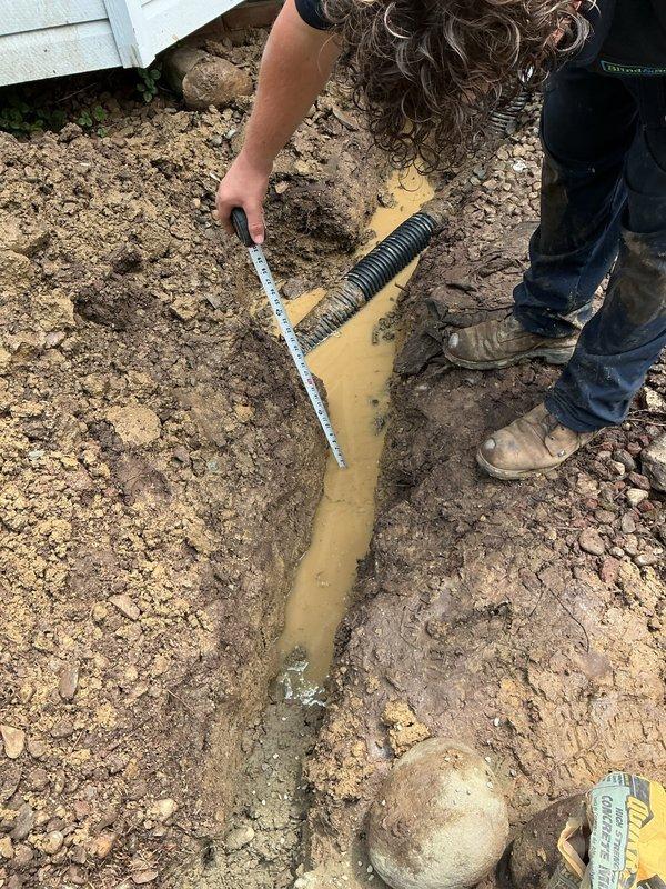 Assessed damaged underground electrical line to post light that was struck during sidewalk installation. Existing line was temporarily repaired but requires complete replacement to meet code requirements. Sidewalk company installed conduit at insufficient depth (3 inches); code requires 12-inch burial depth throughout run with GFCI protection.

Scope of work includes breaking out concrete surrounding existing post light fixture, which may require complete fixture replacement due to concrete damage. Will salvage light head if possible but post assembly likely compromised. New circuit will originate from right side of home near garage at existing line location. Installation plan: disconnect existing circuit inside home, install nail-on box with GFCI device at interior wall, exit home at same penetration point, run new underground line approximately 8 feet to relocated post light position clear of concrete sidewalk area. All excavated trenches will be backfilled; final landscaping grading