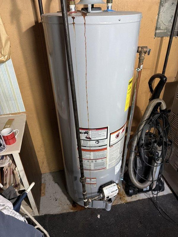 Responded to service call for leaking conventional tank-style water heater. Upon arrival, inspected unit and identified significant rust staining on exterior of tank with active leaking from bottom of vessel. Documented condition with photographs showing vertical rust streaks indicating corrosion and tank failure. Explained to customer that tank-style water heater had reached end of service life and replacement was necessary, as bottom leaks indicate internal tank deterioration that cannot be repaired.