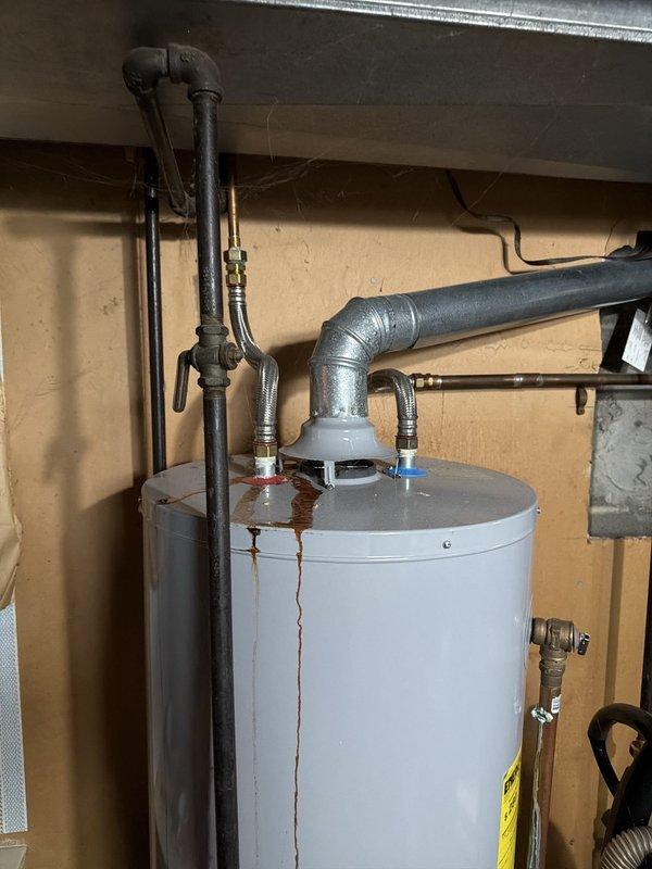 Responded to service call for leaking conventional tank-style water heater. Upon arrival, inspected unit and identified significant rust staining on exterior of tank with active leaking from bottom of vessel. Documented condition with photographs showing vertical rust streaks indicating corrosion and tank failure. Explained to customer that tank-style water heater had reached end of service life and replacement was necessary, as bottom leaks indicate internal tank deterioration that cannot be repaired.