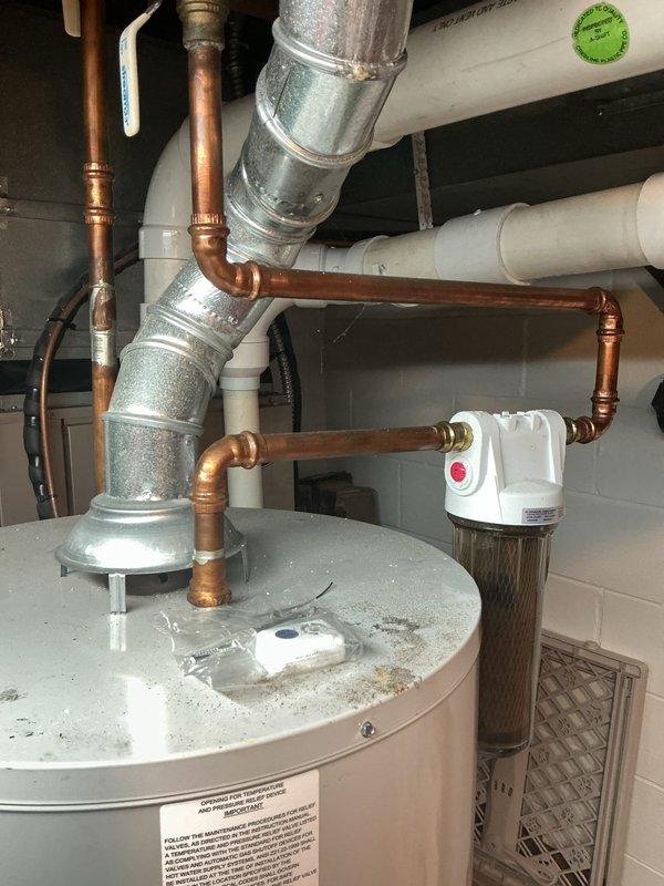 Conducted on-site assessment of existing Bradford White Defender Safety System water heater to provide replacement estimate. Documented current installation configuration including copper supply line connections, galvanized venting system, and associated plumbing infrastructure. Photographed water heater condition, showing accumulated debris on top surface, existing pipe routing with multiple elbow fittings, PVC drain lines, and adjacent water treatment equipment. Evaluated accessibility, clearances, and existing connections to determine scope of replacement work required.