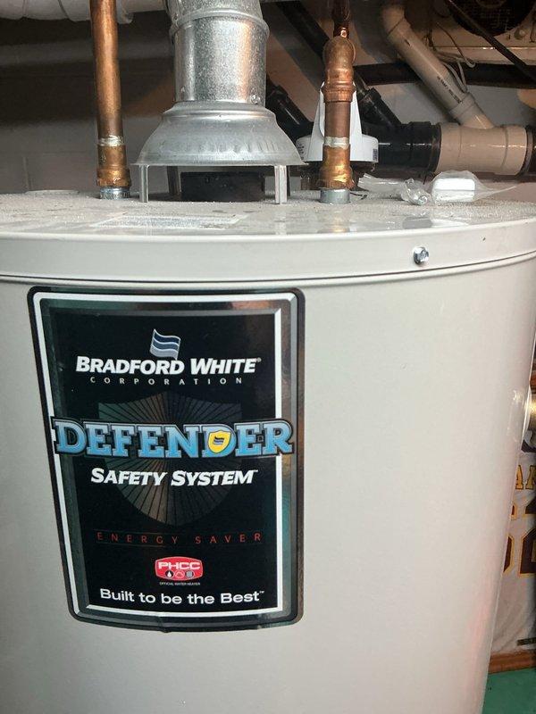 Conducted on-site assessment of existing Bradford White Defender Safety System water heater to provide replacement estimate. Documented current installation configuration including copper supply line connections, galvanized venting system, and associated plumbing infrastructure. Photographed water heater condition, showing accumulated debris on top surface, existing pipe routing with multiple elbow fittings, PVC drain lines, and adjacent water treatment equipment. Evaluated accessibility, clearances, and existing connections to determine scope of replacement work required.