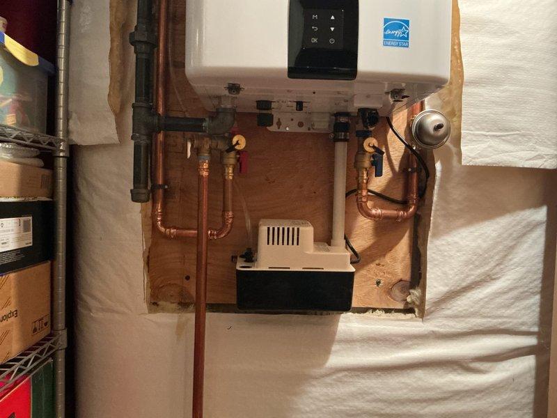 Completed installation of Navien 240 tankless water heater system with buffer tank and recirculation capability. Mounted unit on plywood backing with proper venting, connected copper supply and return lines with isolation valves, installed expansion tank, and integrated condensate neutralizer system with newly added condensate pump for proper drainage. All components professionally staged, piped with brass fittings, and tested for proper operation alongside existing HVAC system in basement utility area.