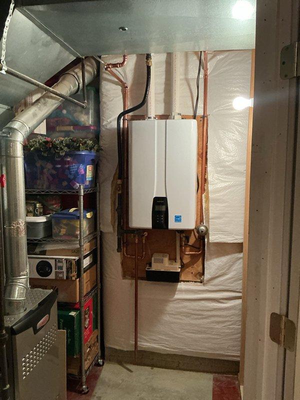 Completed installation of Navien 240 tankless water heater system with buffer tank and recirculation capability. Mounted unit on plywood backing with proper venting, connected copper supply and return lines with isolation valves, installed expansion tank, and integrated condensate neutralizer system with newly added condensate pump for proper drainage. All components professionally staged, piped with brass fittings, and tested for proper operation alongside existing HVAC system in basement utility area.