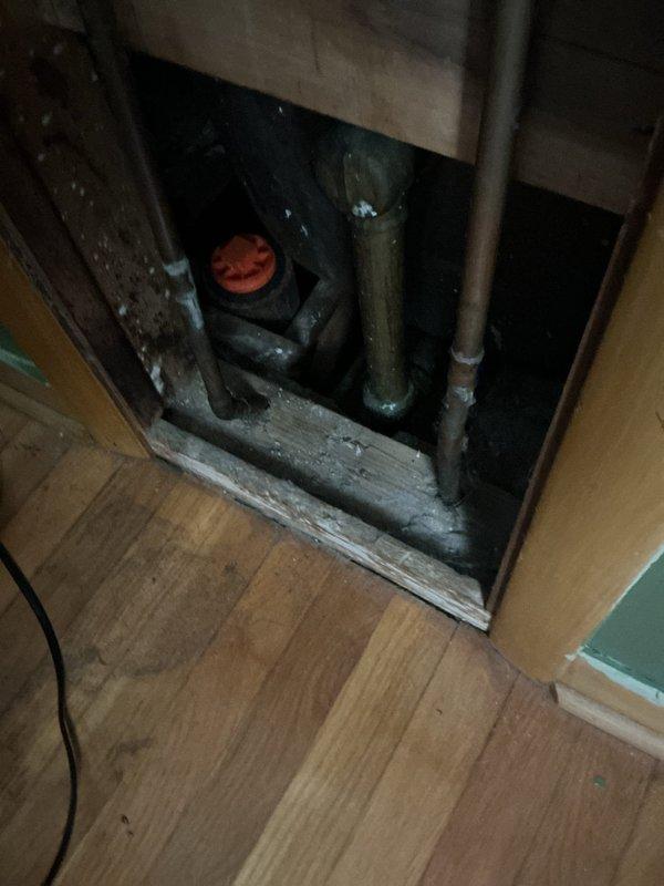 Responded to upstairs bathtub drainage issue. Upon arrival, found bathtub with standing water and damaged drain assembly with red rubber component protruding from drain opening. Accessed plumbing system through floor access panel to inspect drain line and shutoff valves. Removed defective drain stopper mechanism and cleared obstruction from drain line. Tested drainage flow and verified proper operation of bathtub drain system.