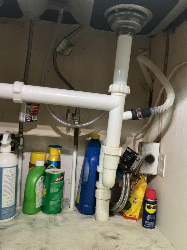Responded to service call for toilet leak causing water to trickle down drain pipe and form puddles on basement floor. Inspected vertical cast iron waste stack in basement where pipe passes through floor joists, identifying leak at collar connection point during flush cycles. Examined under-sink plumbing and drain connections to assess overall drainage system condition in 70-year-old home. Documented existing pipe conditions including aged cast iron stack with visible corrosion at flanged joint section. Photographed leak source area and related plumbing infrastructure for assessment and recommended repairs to address water intrusion issue.