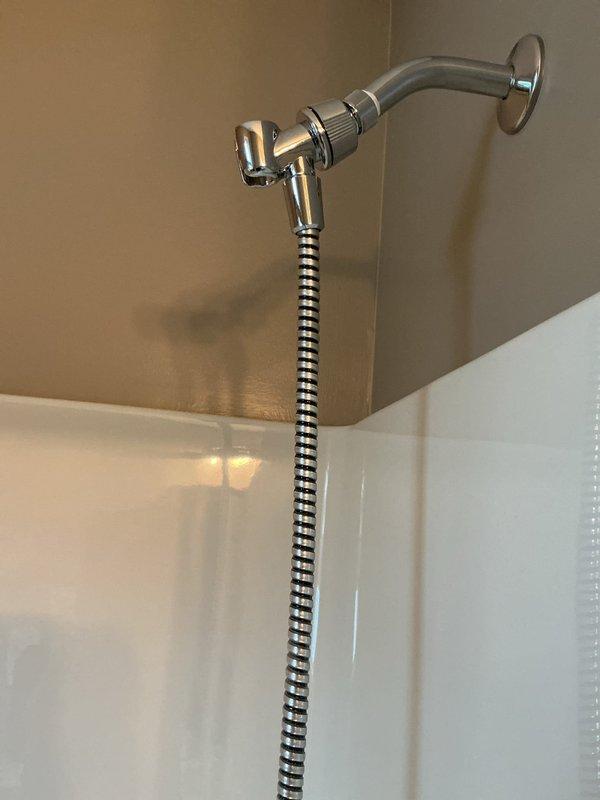 Responded to service call for malfunctioning handheld shower head with water leaking from multiple points at the wall connection and hose attachment to spray handle. Removed defective unit and installed new chrome-finished handheld shower head assembly with flexible metal hose and adjustable wall-mounted bracket. Tested installation to verify proper water flow and confirmed no leaks at connection points.