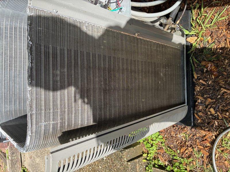 Completed MVP cooling maintenance visit on residential HVAC system. Upon inspection, discovered significant debris accumulation between evaporator coil assemblies, including dead leaves, dirt, and organic matter concentrated in the lower section where coil units meet. Observed heavy dirt and dust buildup covering substantial portions of the outdoor condenser unit coils, with visible discoloration across center and right sections contrasting with cleaner metallic fins on left side. Documented deterioration along coil edge with fraying material present. Unit showed signs of weathering and required cleaning to restore optimal heat exchange efficiency and system performance.