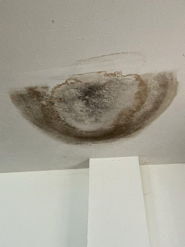 Responded to a water leak originating from a second-floor toilet that was causing damage to the garage ceiling below. Upon inspection, discovered extensive water staining and discoloration on the garage ceiling with dark brown and black concentrated areas indicating active moisture infiltration. Removed the toilet and found a severely deteriorated toilet flange with significant corrosion on the mounting bolts, degraded wax ring, and water damage to the surrounding floor area with visible mineral deposits and efflorescence. The flange showed heavy wear, rust, and compromised sealing materials that allowed water to bypass the fixture and penetrate through the floor assembly into the space below. Performed diagnostic assessment and documented the conditions with photographs for repair recommendations.
