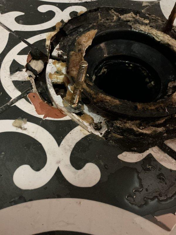 Responded to a water leak originating from a second-floor toilet that was causing damage to the garage ceiling below. Upon inspection, discovered extensive water staining and discoloration on the garage ceiling with dark brown and black concentrated areas indicating active moisture infiltration. Removed the toilet and found a severely deteriorated toilet flange with significant corrosion on the mounting bolts, degraded wax ring, and water damage to the surrounding floor area with visible mineral deposits and efflorescence. The flange showed heavy wear, rust, and compromised sealing materials that allowed water to bypass the fixture and penetrate through the floor assembly into the space below. Performed diagnostic assessment and documented the conditions with photographs for repair recommendations.