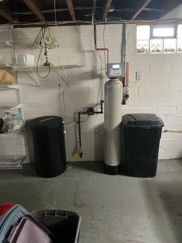 Responded to service call for slow-draining bathtub and garbage disposal evaluation, along with dishwasher hookup inspection. Performed comprehensive 24-point plumbing inspection of the residential property. Assessed basement plumbing infrastructure, including water treatment system with softener tank and filtration components. Inspected bathroom sink drain showing visible rust staining and mineral buildup around drain assembly, indicating potential corrosion issues and need for fixture maintenance. Evaluated all requested plumbing fixtures and connections to identify drainage concerns and verify proper dishwasher installation. Documented existing conditions with photographic evidence for service records.