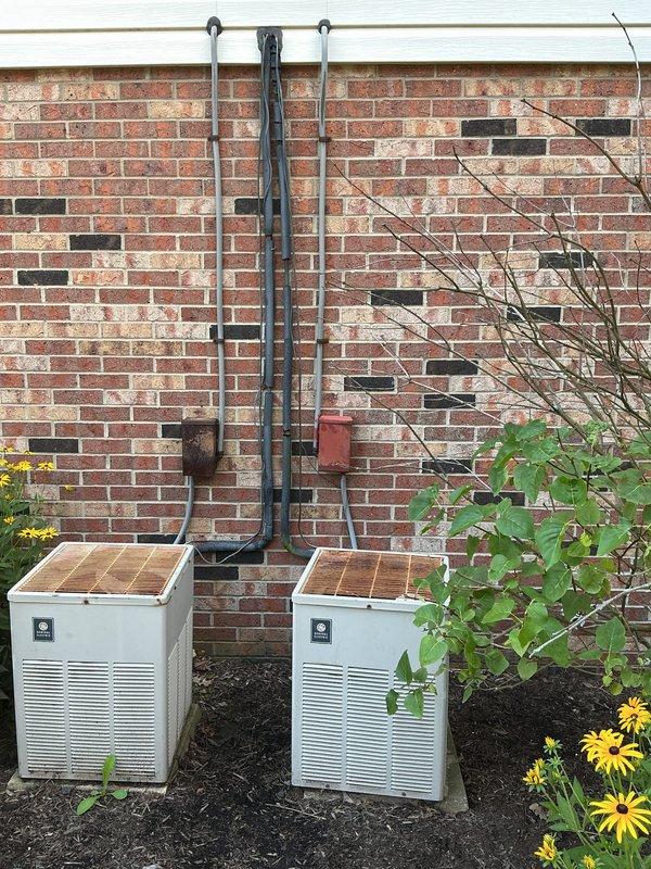 Completed installation of dual A/C units with corresponding evaporator coils in a residential property. Mounted two condenser units on exterior foundation pad against brick wall with proper spacing and leveling, installed refrigerant line sets and electrical conduit secured to building exterior, and connected both systems to existing Amana furnace infrastructure in basement. All refrigerant lines were properly insulated, electrical connections were made to code, condensate drains were installed, and both systems were charged, tested, and verified for proper operation.