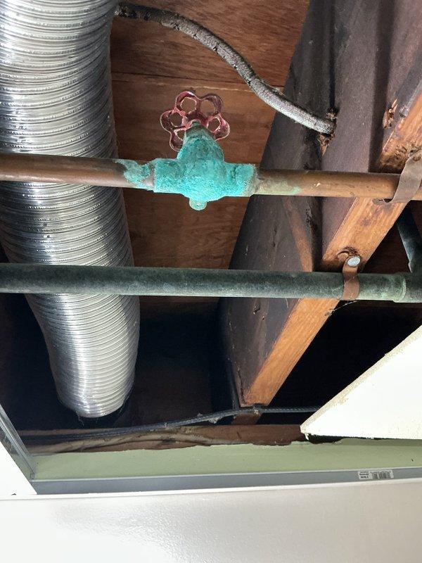 Responded to a broken copper pipe repair in an accessible drop ceiling space. Removed and replaced a corroded section of copper piping that showed significant oxidation and verdigris buildup around the valve fitting area. The deteriorated pipe segment was cut out and a new copper pipe section was installed using proper compression fittings, ensuring secure connections and proper alignment with existing plumbing infrastructure. All work was completed within the wooden joist framework alongside existing HVAC ductwork, with minimal disruption to surrounding systems.