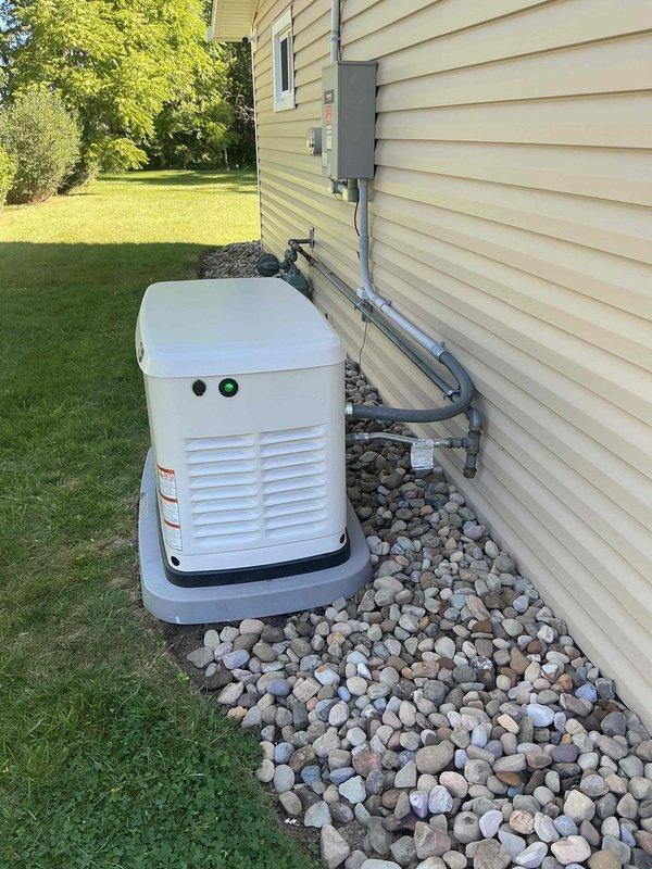 Completed annual maintenance on a one-year-old Generac standby generator installed on composite pad with river rock landscaping. Performed routine inspection of unit including verification of proper operation, checking oil levels, inspecting air filter, testing battery connections, and verifying control panel indicators. Confirmed all ventilation louvers were clear of debris, inspected electrical conduit connections to disconnect box, and verified proper grounding. Unit operational with green status indicator illuminated upon completion of service.