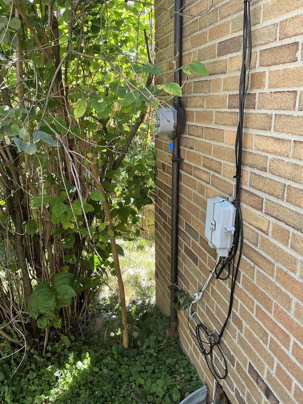 Completed on-site assessment for residential backup generator installation. Evaluated existing electrical infrastructure including main service panel with adequate breaker capacity and documented exterior electrical components and conduit routing on building exterior. Photographed current electrical panel configuration showing main breaker and circuit distribution, as well as exterior mounting locations along brick wall with existing weatherproof enclosures. Assessed optimal placement for generator transfer switch installation and determined routing path for new electrical connections from proposed generator location to main service panel.