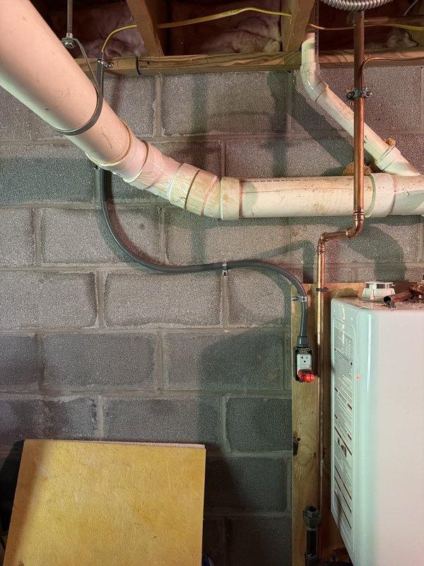 Installed dedicated electrical circuit for tankless water heater system in basement utility area. Routed conduit and wiring through exposed floor joists alongside existing plumbing infrastructure, ensuring proper clearances from PVC drain lines and copper water supply pipes. Circuit installation completed and ready for tankless unit connection and final inspection.