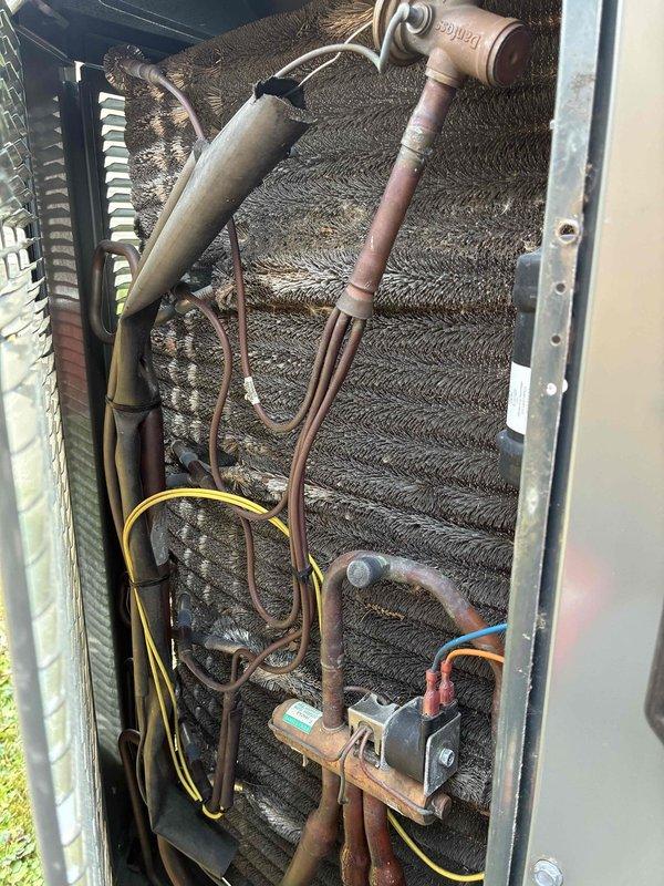 Completed MVP recurring cooling maintenance visit on residential HVAC system. Performed comprehensive inspection of both indoor evaporator coil unit and outdoor condensing unit. Evaporator coil exhibited significant accumulation of dust, dirt, and debris throughout aluminum fins, restricting airflow and reducing system efficiency. Documented condition of refrigerant lines showing age-related oxidation on bare copper sections. Verified all electrical connections, wiring harnesses, and control components including capacitor, compressor motor, and control board. All electrical components found secure with proper connections maintained. Outdoor unit access panel opened for full inspection of compressor, electrical components, and refrigerant line connections. System operational at time of service with all major components functioning. Photographic documentation captured for maintenance records showing current condition of evaporator coil contamination and overall system status.