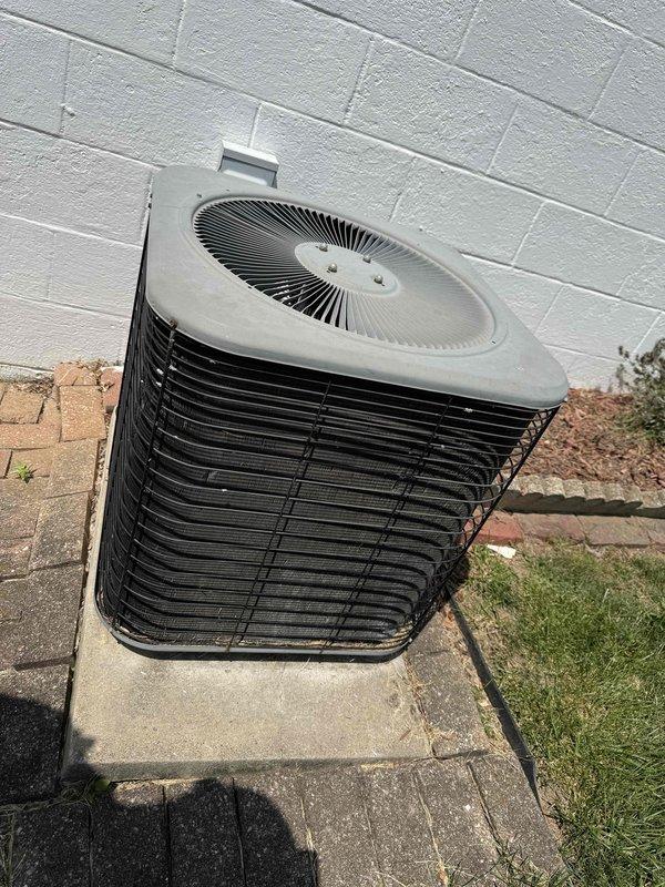 Completed routine MVP cooling maintenance visit on 20-year-old outdoor air conditioning system. Performed comprehensive inspection of cylindrical condenser unit, examining horizontal metal fins for damage and verifying proper airflow through radial fan grille assembly. Inspected electrical panel and control box, checking all wire connections including red, orange, yellow, purple, black, and green conductors secured with proper bundling. Verified capacitor mounting and electrical integrity, noting weathered but functional condition consistent with system age. Examined terminal blocks and connection points for secure attachment and proper operation. Unit operating within normal parameters for age and condition, with condenser positioned appropriately on concrete pad with adequate clearance from structure.