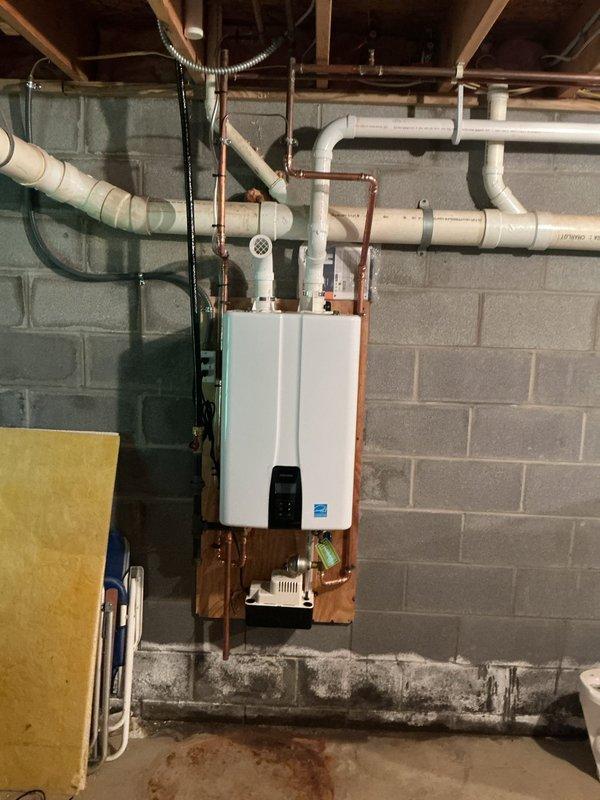 Replaced an 80-gallon AO Smith electric water heater experiencing severe corrosion with a new Navien NPE-240A2 tankless water heater. Connected gas supply to existing 1-inch main trunk line and mounted unit in utility area. Core drilled through brick exterior wall at front of house for proper venting and exhaust installation. Installed condensate pump with discharge line routed to furnace drain location. Coordinated electrical conversion from 240V to 110V service. All copper supply lines connected, system tested and operational.