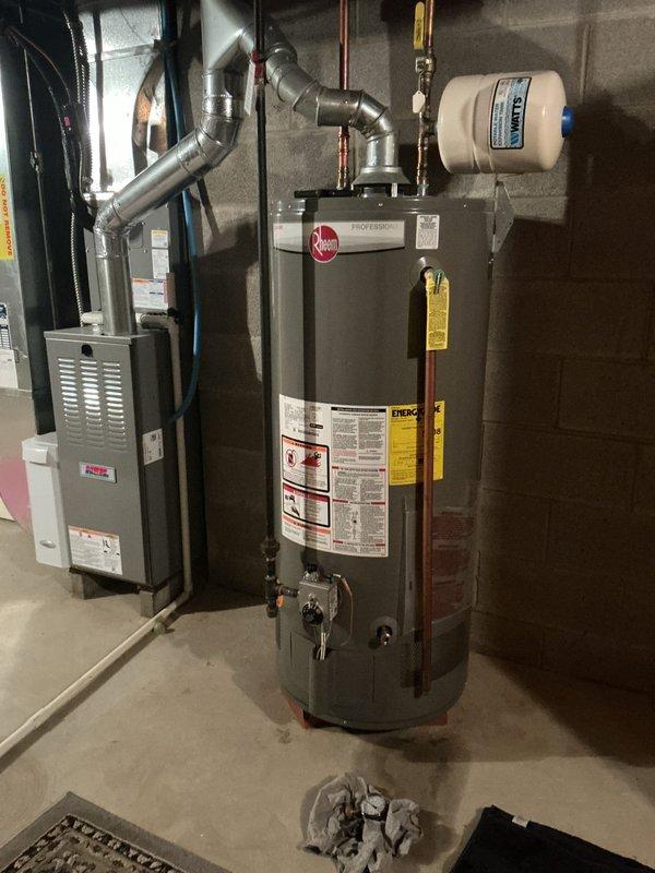 Responded to service call for leaking water heater. Upon arrival, performed diagnostic inspection of residential tanked water heater located in basement utility area. Confirmed active leak originating from bottom of tank, indicating internal tank failure. Water heater identified as Rheem Professional Series unit of unknown age with significant corrosion and deterioration at base. Documented equipment condition with photographs showing compromised tank integrity, existing plumbing connections including copper supply lines, temperature and pressure relief valve, expansion tank, and proximity to HVAC furnace system. Advised customer that bottom tank leaks are non-repairable and require complete water heater replacement due to structural failure of inner tank lining. Provided replacement options and recommendations for new installation.