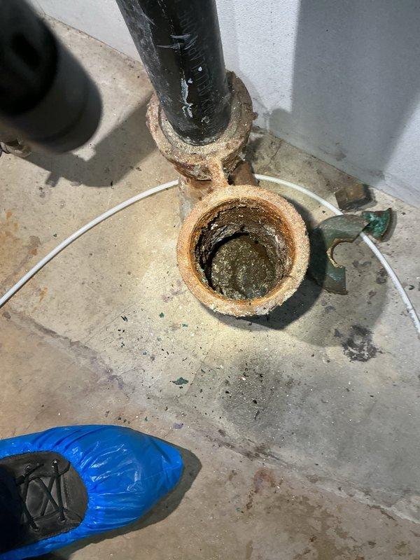 Responded to basement drain backup from clothes washer. Upon inspection, discovered heavily corroded cast iron drain fitting and pipe assembly with significant rust deterioration and internal buildup causing drainage obstruction. Cleared blockage from drain line, removed debris and sediment accumulation from fitting interior. Tested drain flow and verified proper drainage from washer discharge. Documented existing corrosion on pipe assembly and recommended future replacement of deteriorated fittings to prevent recurrence.