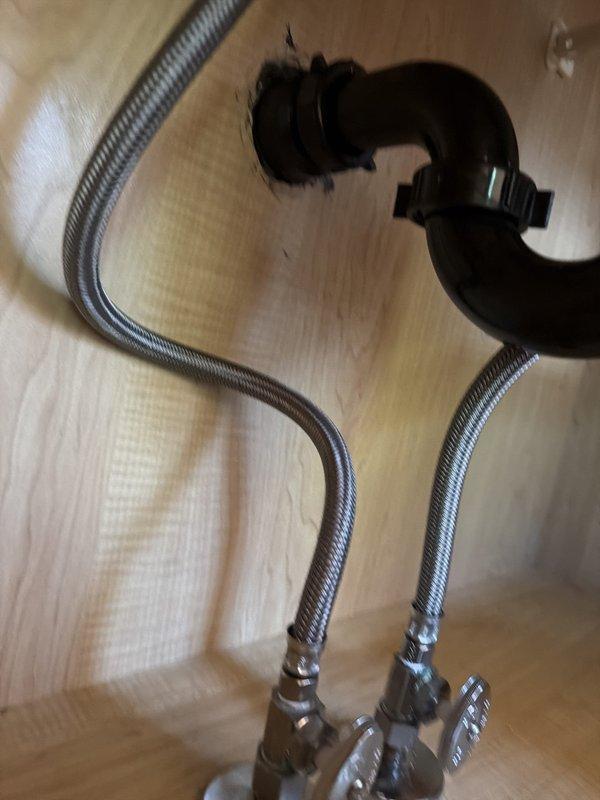 Accessed cabinet interior by opening back panel to repair drain assembly on left side lavatory. Replaced flexible braided supply lines with shut-off valves on right side lavatory, installing new chrome-finished connections. Cleared obstruction from shower drain to restore proper drainage flow.