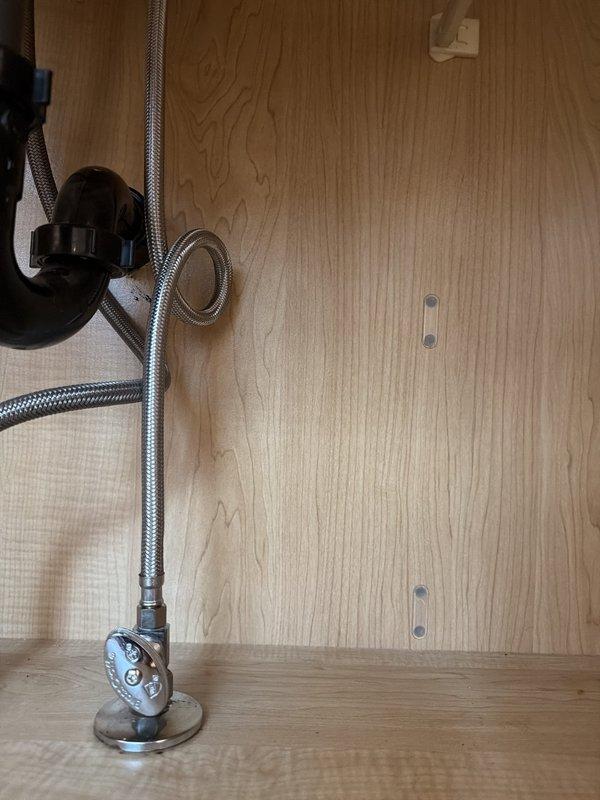 Accessed cabinet interior by opening back panel to repair drain assembly on left side lavatory. Replaced flexible braided supply lines with shut-off valves on right side lavatory, installing new chrome-finished connections. Cleared obstruction from shower drain to restore proper drainage flow.