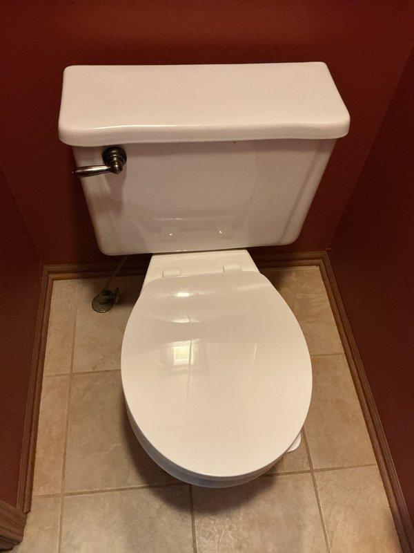 Completed toilet replacement in 40-year-old residential property. Removed existing two-piece toilet fixture from powder room with burgundy walls and beige ceramic tile flooring with decorative border trim. Disconnected water supply line and unbolted toilet from floor flange. Hauled away old toilet per customer request. Inspected floor flange and wax ring seat for proper condition. Installed customer-supplied white porcelain two-piece toilet with chrome flush handle. Secured unit to floor flange with new closet bolts and wax ring seal. Reconnected water supply line and tested for proper flush operation and leak-free connections. Verified proper bowl water level and tank refill function. Cleaned work area and confirmed satisfactory installation with customer.