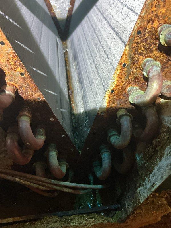 Performed assessment on 17-year-old air conditioning unit experiencing electrical drainage issue affecting furnace control board. Inspected outdoor condenser unit and identified extensive corrosion on mounting brackets, refrigerant lines, and heat exchanger coils. Documented severe rust deterioration on copper tubing, connection points, and equipment housing, indicating prolonged exposure to moisture and environmental elements. Photographed corroded components including serpentine coil assembly, mounting hardware, and electrical wiring pathways. Due to advanced age of system and extent of corrosion damage posing risk to furnace electronics, discussed repair versus replacement options with customer for final decision.