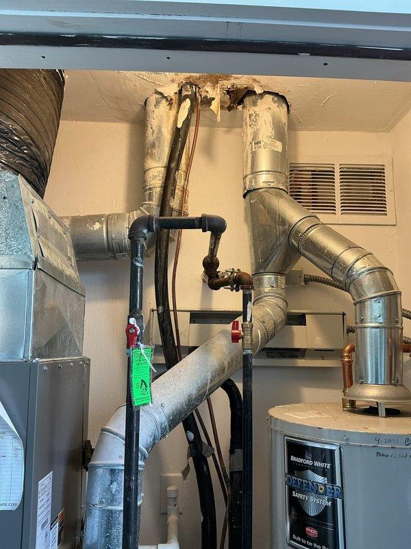 Responded to water leak investigation in mechanical utility room. Upon inspection, confirmed leak was not related to AC system as initially suspected. Identified significant water damage and staining on ceiling around pipe penetrations, indicating active or historical water intrusion from plumbing system. Examined water heater installation, associated piping connections, and overhead plumbing runs. Documented conditions with photographs showing ceiling deterioration, pipe configuration, and equipment layout for further assessment and repair planning.