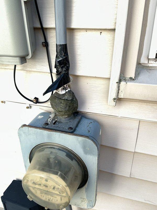 Responded to service call for weatherhead reattachment and securing at residential electrical service entrance. Upon arrival, found the weatherhead and service mast connection point had separated from the building, with the overhead service conductors under stress and the weatherhead junction showing signs of deterioration with weathered electrical tape on the conduit. Reattached and properly secured the weatherhead assembly to the exterior wall, ensuring adequate support for the service entrance conductors. Verified proper clearances and mechanical connections at the meter base and service entrance equipment. Replaced deteriorated tape and securing hardware on the gray conduit extending from the weatherhead to the meter enclosure. Confirmed all electrical connections remained intact throughout the meter base, disconnect, and main service panel. Tested system operation and verified stable mounting of all service entrance components to prevent future detachment issues.