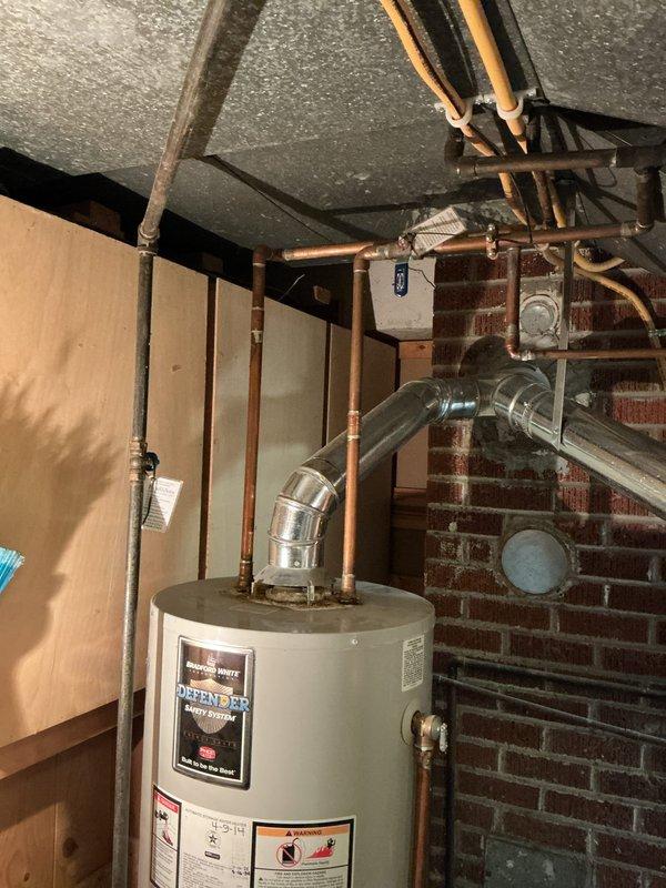 Conducted on-site assessment of existing 50-gallon gas water heater located in basement utility area for replacement estimate. Evaluated current installation including copper supply lines, gas connections, exhaust venting system with metallic flue pipe, and clearance specifications in confined space between wood-framed partition and exposed brick wall. Documented unit specifications, manufacturer information, and existing plumbing configuration with copper piping connections at top of unit. Photographed installation conditions, surrounding infrastructure, and access points to provide accurate replacement quote for new 50-gallon gas water heater with comparable specifications and code-compliant installation requirements.