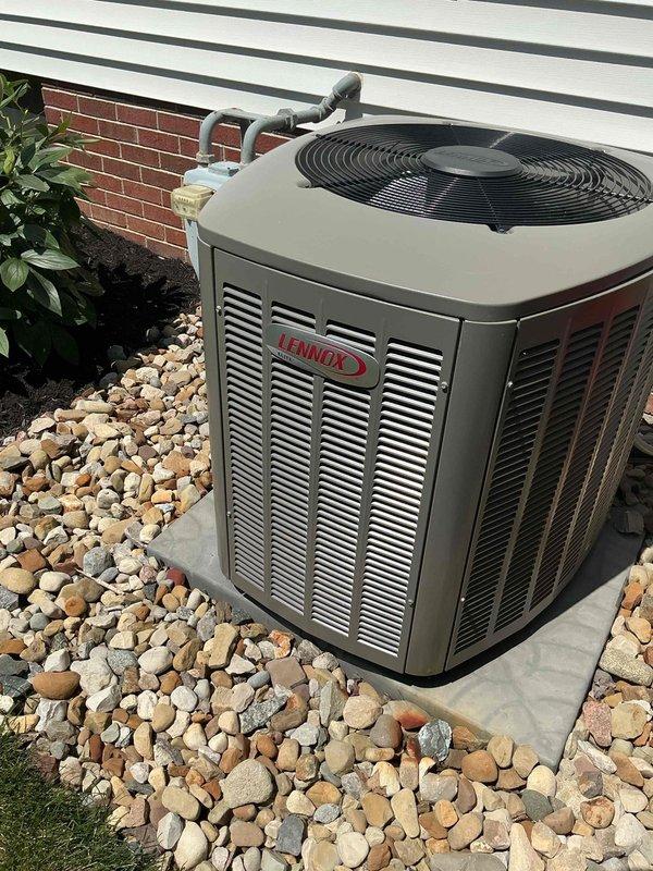 Responded to service call for non-operational air conditioning system affecting entire home. Upon arrival, inspected 4-year-old Lennox condensing unit located on exterior concrete pad with proper clearances and landscaping. Unit remained under manufacturer warranty from original installation. Performed comprehensive diagnostic evaluation of outdoor condenser including visual inspection of housing, louvered panels, and fan assembly. Checked electrical disconnect box and conduit connections mounted on building exterior. Verified refrigerant line sets running from condenser to structure showed no visible damage or degradation. Assessed unit positioning on concrete pad and surrounding river rock landscaping for proper drainage and airflow clearance. Documented equipment condition and installation configuration with photographs for warranty claim processing and service records. System required warranty service authorization to proceed with necessary repairs.