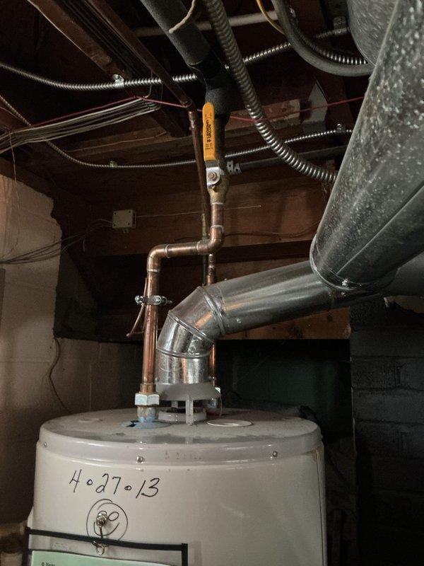 Responded to service call for water heater replacement in residential property originally constructed in 1950. Upon arrival, conducted thorough assessment of existing water heater installation located in basement utility area. Documented existing unit condition through photographic inspection, noting handwritten installation date marking of "4-27-13" on tank exterior, indicating approximately 11-year-old equipment at end of serviceable life.

Evaluated existing plumbing configuration including galvanized and copper supply line connections, vent pipe assembly, and relief valve installation. Assessed surrounding utility space constraints including exposed floor joists, existing HVAC ductwork, concrete block foundation walls, and available clearances for equipment replacement. Verified electrical and gas connections as applicable to existing installation.

Prepared comprehensive estimate for complete water heater replacement including removal and proper disposal of existing unit, installa