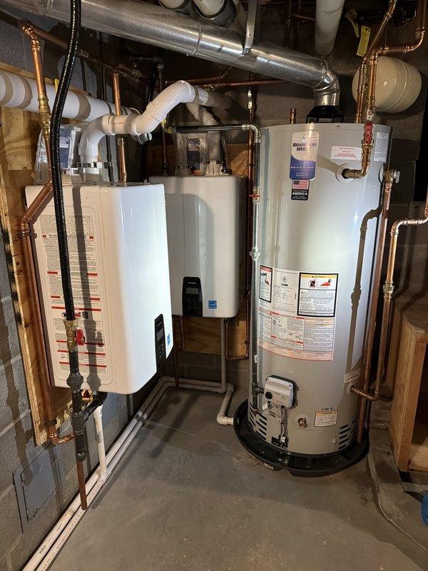 Completed installation of two Navien tankless water heaters for domestic hot water supply and one 50-gallon conventional water heater dedicated to space heating system. Replaced failed temperature and pressure relief valve on existing water heater and adjusted thermostat setting to hot position. Installed new copper supply lines and white PVC venting system throughout basement mechanical room, routing pipes through floor joists with proper support brackets and hangers. Connected both tankless units to existing gas supply and electrical systems, mounting units on basement wall per manufacturer specifications. Configured plumbing system to separate domestic hot water production from hydronic heating loop. All connections pressure tested and verified for proper operation. Protected customer's carpeted areas with floor runners during equipment transport and installation. Two-day installation completed with helper assistance.