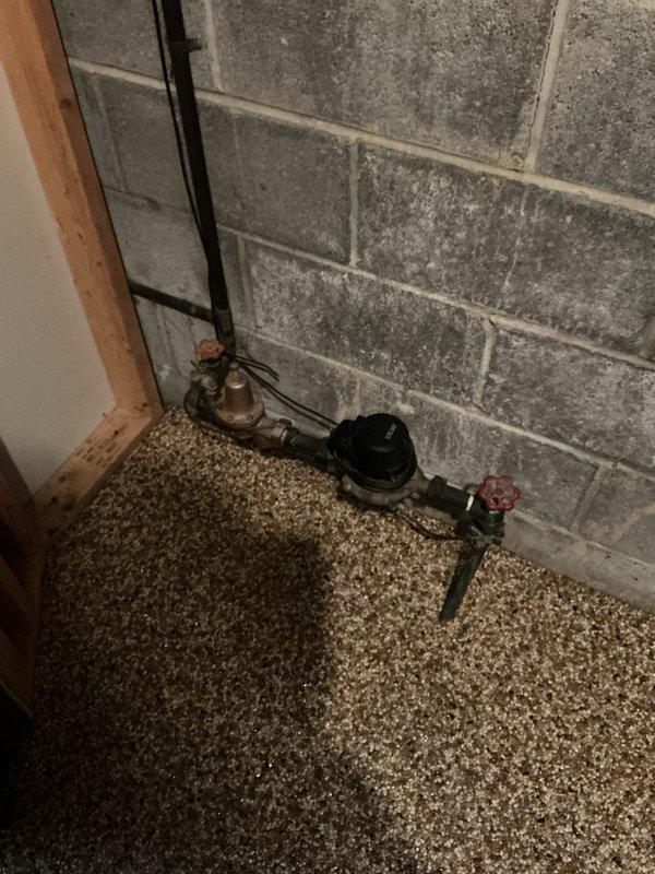 Responded to service call for leaking outdoor spigot at a 50-year-old residential property. Upon arrival, assessed the exterior hose bib and associated plumbing connections. Documented existing water meter assembly in basement with shutoff valves showing signs of age and corrosion. Inspected outdoor spigot mounted on exterior vinyl siding and identified source of leak. Photographed plumbing infrastructure including water meter, shutoff valves, and exterior fixture for estimate preparation. Provided detailed assessment and repair recommendations to address the leaking outdoor spigot.