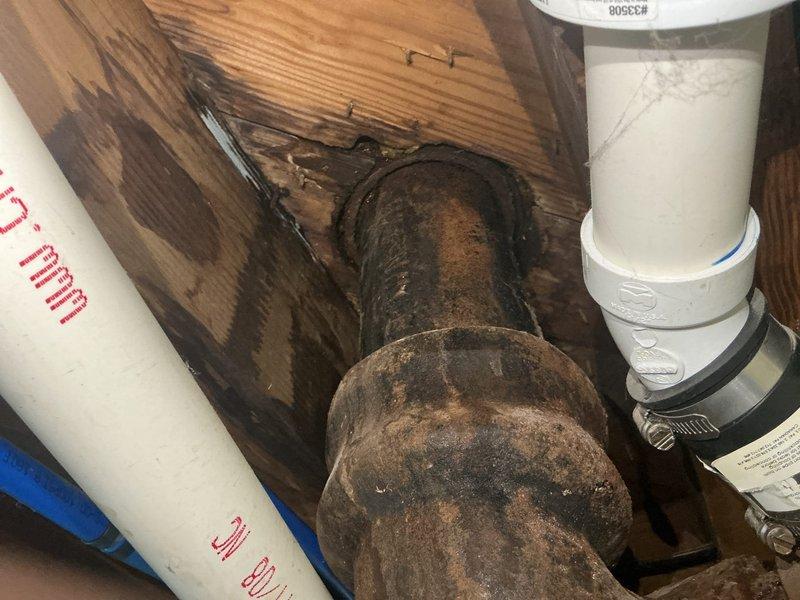 Responded to complaint of sewage odor emanating from basement floor drain during washing machine drainage cycles and suspected toilet leak. Upon inspection of 1940s-era home, identified severely corroded cast iron or galvanized waste piping in basement mechanical room showing advanced deterioration with rust scaling and pitting. Observed evidence of chronic moisture infiltration indicated by extensive water staining on adjacent wooden framing members. 

Assessed plumbing system configuration consisting of mixture of original metal piping and newer PVC installations. Floor drain trap likely experiencing siphonage or loss of water seal due to inadequate venting or negative pressure created during washer discharge. Corroded metal drain lines contributing to reduced flow capacity and potential for blockages that exacerbate drainage issues. Documented existing conditions with photographic evidence showing water heater, HVAC equipment, and compromised piping infrastructure. 

Recommended rep